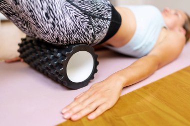 Köpük silindirli fitness egzersizi. Yoga minderi üzerinde spor yapan ve köpük silindir kullanan bir kadın..