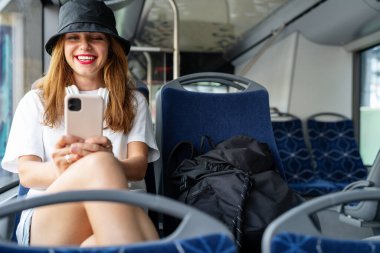 Genç bir kadın otobüste otururken cep telefonunu kullanıyor..