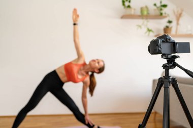 Arka planda bulanık fitness koçunun önünde tripodun üzerindeki video kamera..
