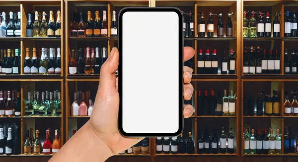 Online service for alcohol delivery. Liquor delivery mobile app mockup. Smart phone with blank screen in front of wine bottles on shelves in store.