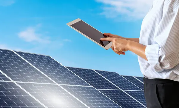 Female person wearing formal outfit controls the solar energy station remotely using a digital tablet.