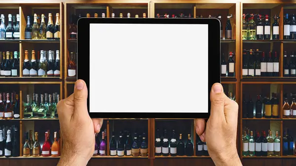 Online service for alcohol delivery. Liquor delivery mobile app mockup. Digital tablet with blank screen in front of wine bottles on shelves in store.