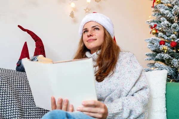 Noel Baba şapkalı yetişkin bir kadın Noel tatili boyunca masal, fantezi ve hayaller okuyor..