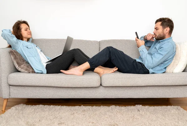 Genç çift evdeki koltukta otururken kişisel bilgi cihazlarını kullanıyor. Çevrimiçi ilişki.