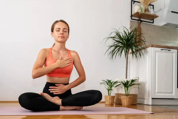 Evde yoga yaparak huzurlu bir meditasyon. Yoga minderinde poz verirken nefes egzersizi yapan bir kadın..