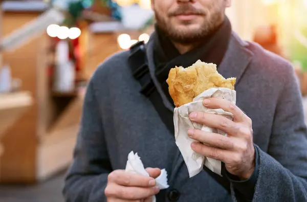 Street food at Christmas Fair. Back to street. Male person eating fast food. Balkans street food