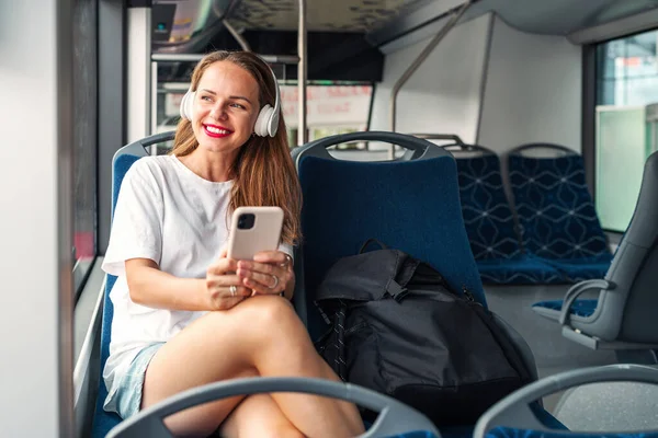 City transportation and passengers lifestyle. Attractive woman listens to a music using her headphones while traveling by bus.