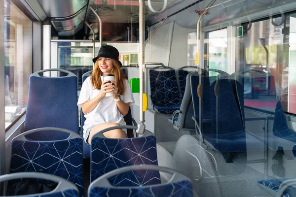 Young woman with travel coffee mug travels by city bus.