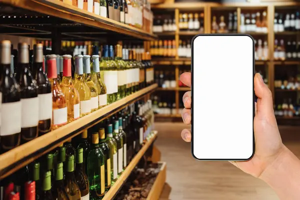 Smart phone with empty screen in female\'s hand in front of liquor store. Online ordering and shopping of alcohol drinks. Mockup for mobile app.