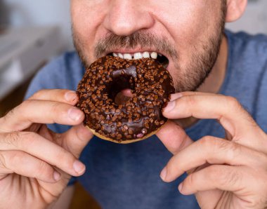 Adam pembe renkli çikolatalı donut yiyor..