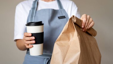 Garsonun elinde hazır yemek. Kahve fincanı ve içinde yiyecek olan bir paket kağıt poşet getir.. 