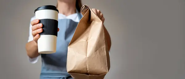 Waitress gives a takeout food order, travel coffee mug and brown paper bag in hands.