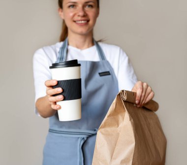 Güzel bir garsonun ellerinde gübre kahve fincanı ve paket yemek paketi. Paket servis için çevre dostu paket.