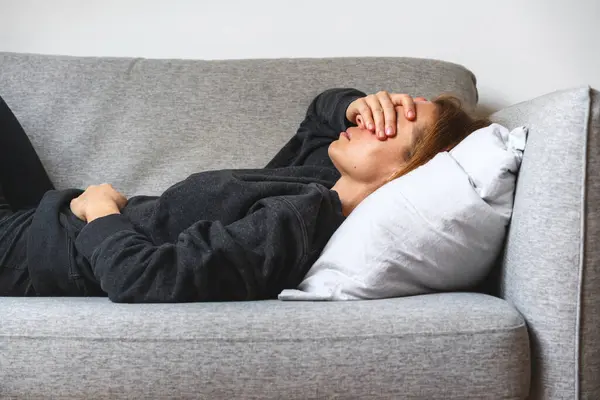 Mutsuz, ümitsiz, depresif bir kadın kanepeye uzanıyor ve elleriyle gözlerini kapatıyor..