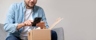 Kot gömlekli bir adam bir paket alıp internetten sipariş verirken fotoğrafını çekiyor. Akıllı telefonunu kullanarak çevrimiçi mağazayla görüşleri paylaşan kişi.