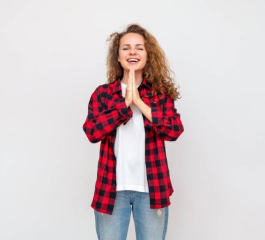 Kırmızı tişörtlü kıvırcık saçlı kadın açık gri bir arka plana karşı neşe ve beklenti duygularını ifade ediyor ve ifade ediyor..