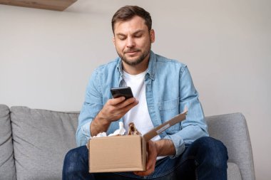 Adam onun online siparişini açıyor ve satın aldıklarının fotoğraflarını çekiyor. Erkek kişi çevrimiçi olarak ekspres teslimat hizmetinin değerlendirmelerini paylaşıyor. E-ticaret.