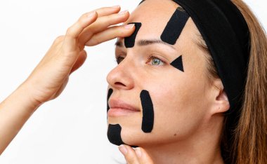 Facial wrinkle reduction and skin lift. Woman beauty model applying black coloured kinesio facial tapes on her face, closeup photography,