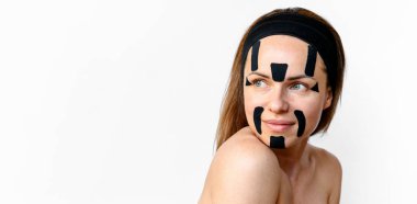 Beauty model with kinesio tapes on her face posing in front go white background in studio. skin care and skin improvement concept.