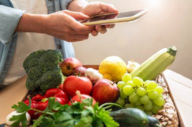 Person buying farm grown organic vegetables online using mobile phone. ordering and delivering grocery products via the internet.