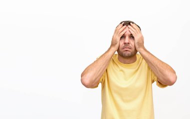 Sarı gömlekli bir adam, elleri başının üstünde, şaşkın ve şaşkın bir ifadeyle yukarı bakıyor. beyaz arkaplanda izole.