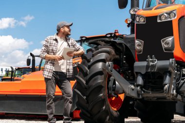 Tarım makineleri bayiliği. Elinde dijital tablet olan bir adam traktöre bakıyor..