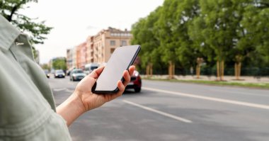 Kadın ellerinde boş ekranlı cep telefonu şehir yolunun arka planında trafik var..