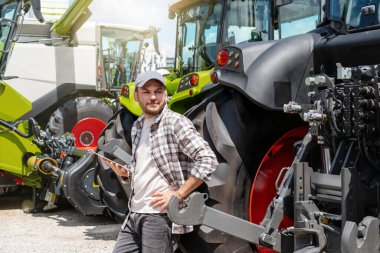 Tarım makinelerinin satışı. Yeni bir çiftlik traktörünün yanında dijital tabletli bir adam.