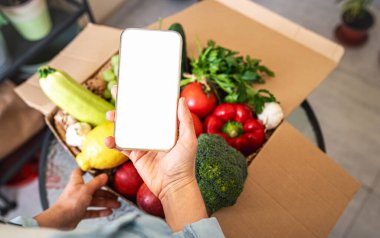 İnternetten sebze ve meyve yetiştiriyorlar. Kadın eli boş cep telefonu ve taze sebzeli karton kutu..