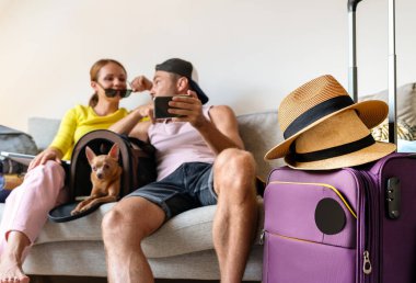 Bulanık arka planda hasır şapkalı seyahat çantası. Küçük köpekli mutlu bir çiftin yaz gezisi için yer ayırtması..