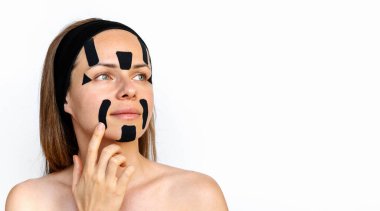 Genç kadın güzellik modeli yüzüne siyah renkli yüz bantları yapıştırıyor..