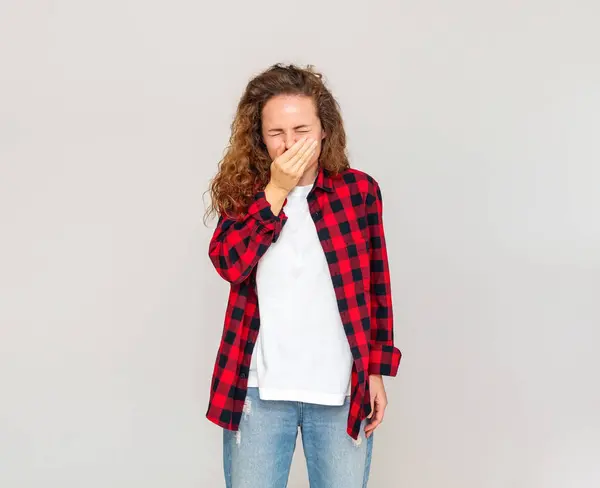 stock image curly woman wearing casual outfit sneezing on plain light grey background. Flu season, allergic reaction, germ spread.