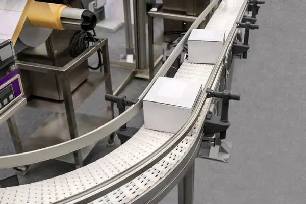 Endüstriyel paketleme ve etiketleme makinesi. Üretim hatlarında beyaz karton kutuların yüksek görünümü.