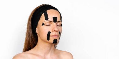 Yüzünde siyah renkli kinesiyoloji bantları olan esmer bir kadın, gözleri kapalı, beyaz arka planda soyutlanmış..