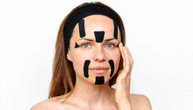 Yüzünde siyah renkli kinesiyoloji bantları olan esmer bir kadın, gözleri kapalı, beyaz arka planda soyutlanmış..