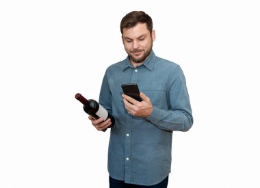 İçki dükkanında şarap seçerken cep telefonuna bakan izole bir erkek müşteri. Adamın elinde şarap şişesi ve akıllı telefonu var..