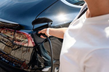 Kadın elektrikli arabasını şarj ediyor. Kadın EV patlayıcı konnektörünü elinde tutuyor..