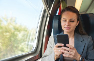 İş kadını kıyafetleri içinde trenle seyahat ederken akıllı telefonunu kullanıyor. İş seyahati ve iş seyahati
