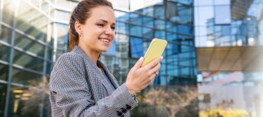 Şirket ağları. İş kadını akıllı telefonuyla üniversitelerle iletişim kuruyor. Ofis binasının dışında akıllı telefon kullanan bir kadın işadamı..