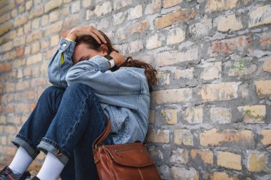 Kadın kıvrılıyor, yerde oturuyor elleriyle yüzünü gizliyor. Derin duygusal sıkıntı ya da depresyon.