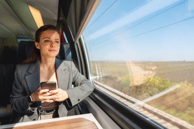 Trenle seyahat ederken akıllı telefon kullanan esmer beyaz kadın. İş kadını ve iş seyahati.