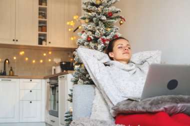 Gözleri kapalı ve elleri başının arkasında olan bir kadın Noel tatilinde koltukta dinleniyor.. 