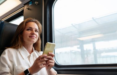 Akıllı telefonlu bir kadın trenle seyahat ediyor. Demiryolu taşımacılığı ve ulaşımı.