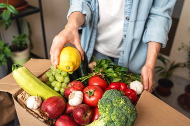 Unpacking a cardboard box with farm-grown organic fruits and vegetables from an online order. Online grocery shopping. clipart