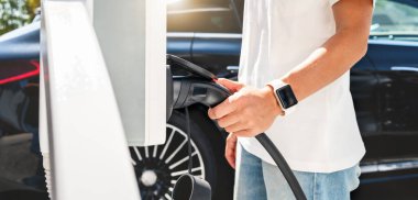 Şehrin şarj istasyonunda elinde elektrikli araba konnektörü olan kadın sürücü. Elektrikli araç şarj altyapısının geliştirilmesi.