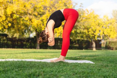 Şehir parkındaki yeşil çimlerde yoga yapan beyaz bir kadın..