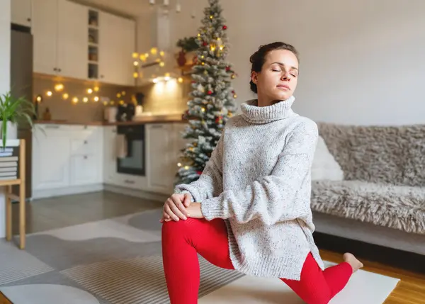 Beyaz kadın Noel tatilinde evde yoga esneme egzersizi yapıyor.. 