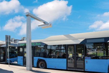 Pantograph charging electric buses station in city in front of summer blur sky. Zero-emission vehicles. clipart