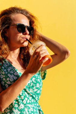 Genç şık şehir kadını sarı duvara karşı pipetle meyve suyu içiyor..