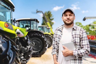 Dijital tabletli adam liderlikte tarım makinelerinin önünde.